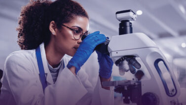 A forensics specialist in a white lab coat peers into a microscope.