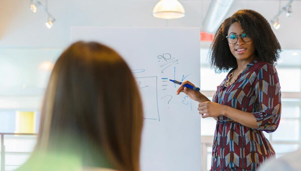 Woman writing on a white board presenting to professional colleagues
